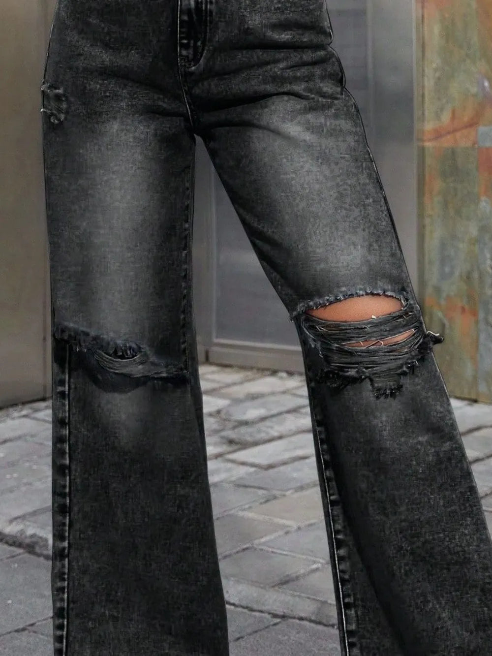Black distressed jeans worn by a person on a stone pavement.