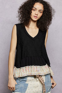 Woman wearing a black sleeveless top with a ruffled, multicolored bottom on a gray background