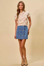 Woman wearing a floral top and denim skirt on a beige background