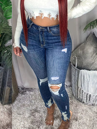 Person wearing ripped blue jeans and a white cropped top in a casual indoor setting.