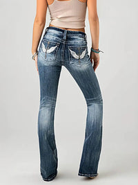 Person wearing blue jeans with decorative stitching on a plain background