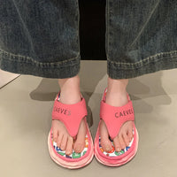 Pink sandals with colorful soles worn by a person in jeans.