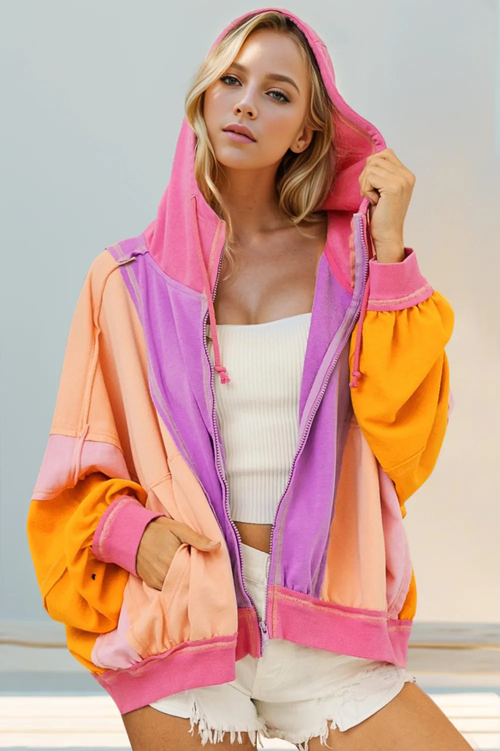 Woman wearing a colorful hoodie with pink, orange, and purple sections against a light background.