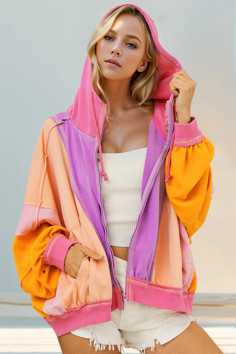Woman wearing a colorful hoodie with pink, orange, and purple sections against a light background.
