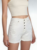 Person wearing white denim shorts and a beige top on a plain background