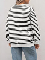 Person wearing a black and white striped sweater with light blue jeans on a plain background