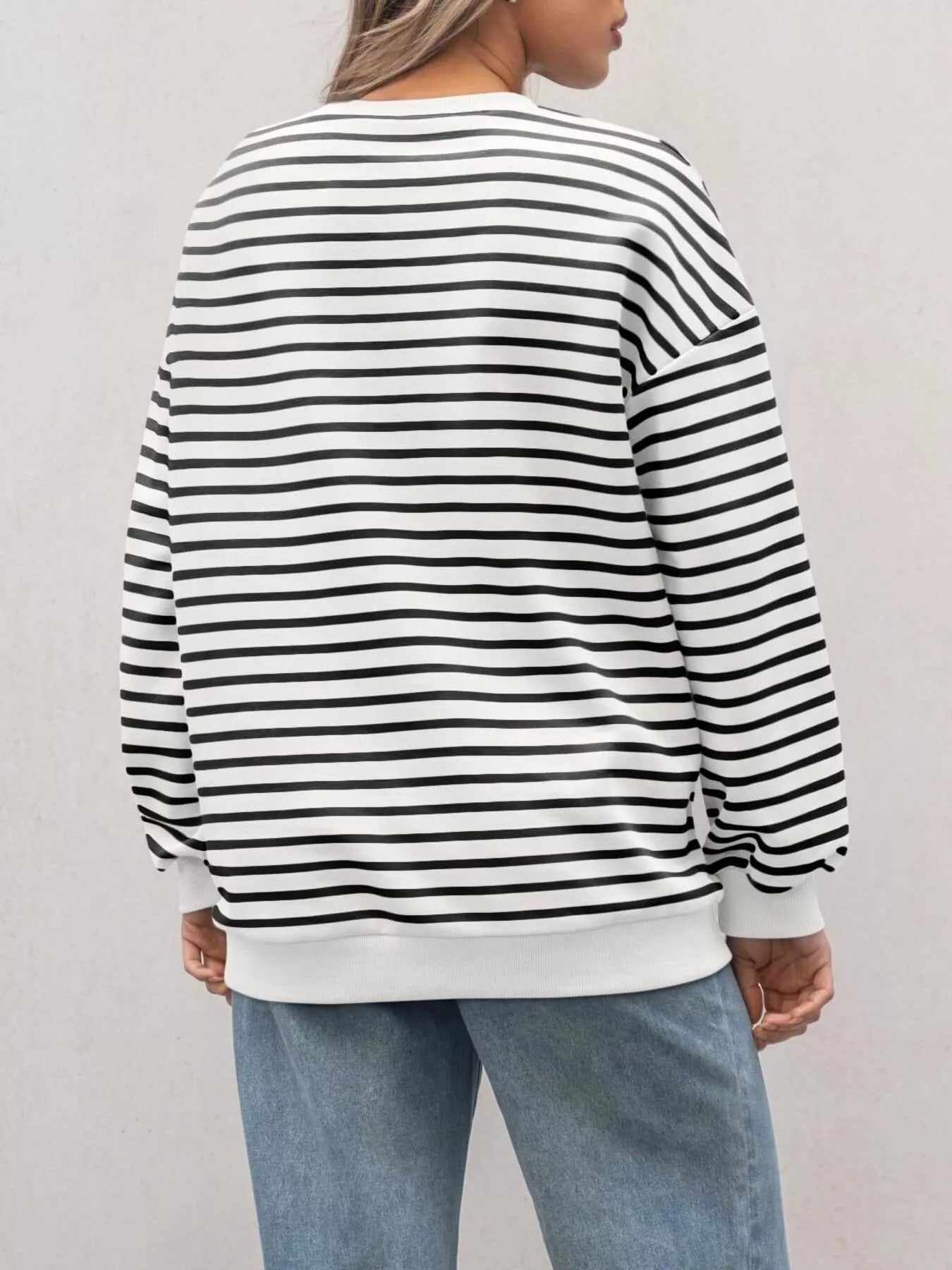 Person wearing a black and white striped sweater with light blue jeans on a plain background
