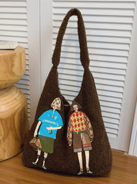 Brown textured handbag with embroidered figures on a wooden surface