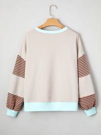 Beige sweatshirt with striped sleeves and cuffs on a hanger against a light gray background