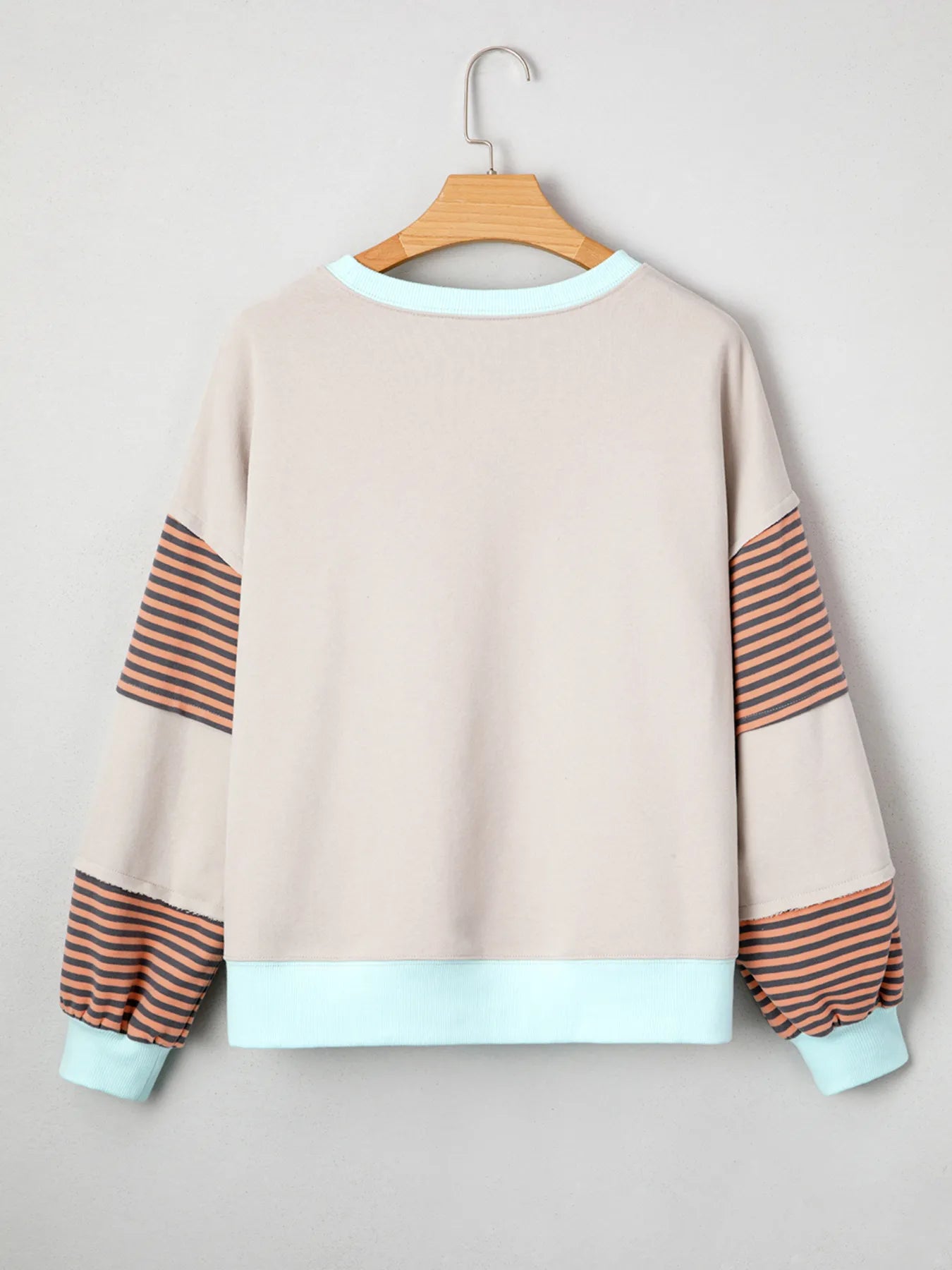 Beige sweatshirt with striped sleeves and cuffs on a hanger against a light gray background