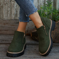 Green ankle boots with zippers worn by a person on wooden steps.