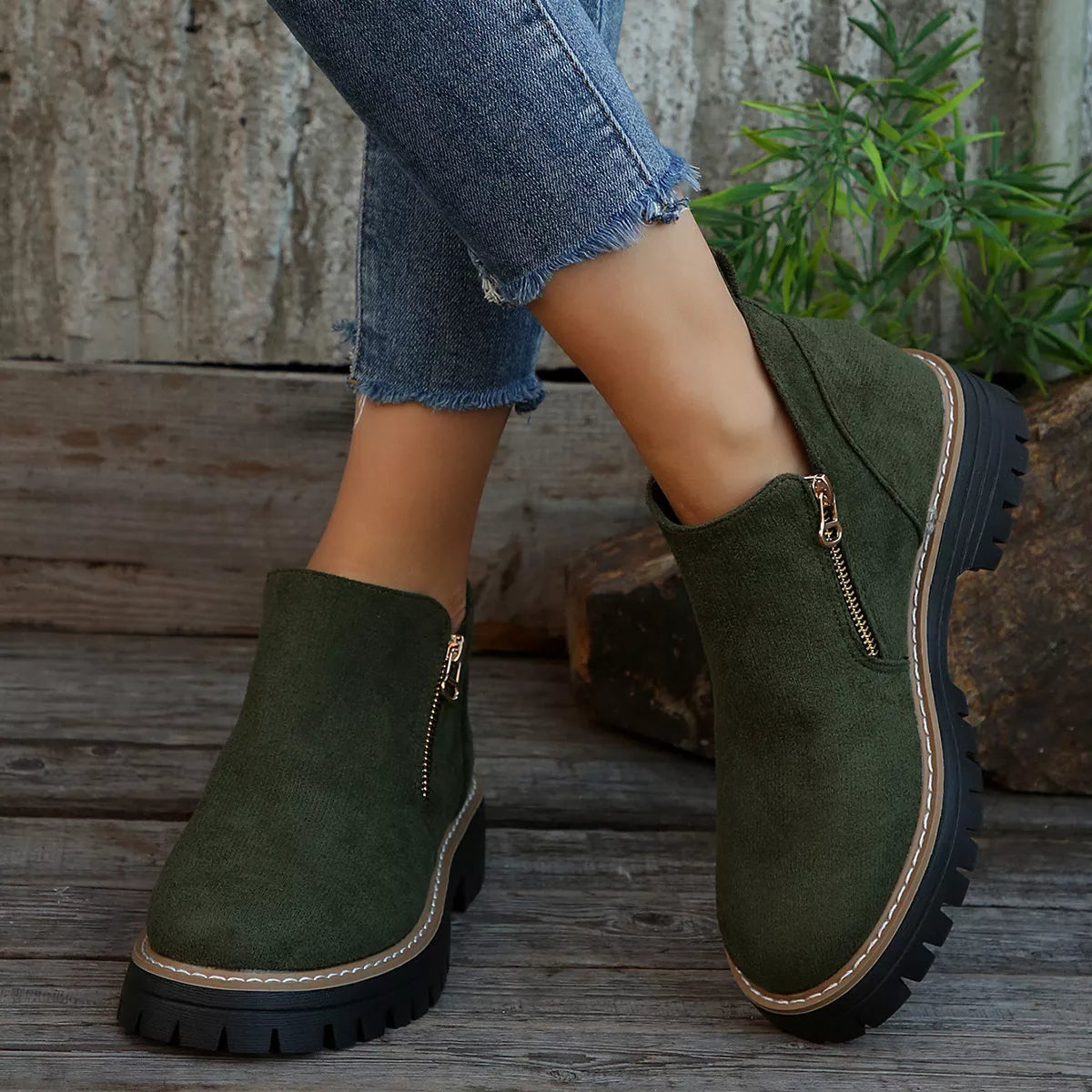 Green ankle boots with zippers worn by a person on wooden steps.