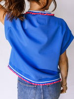 Blue top with pink and white trim worn by a person on a plain background