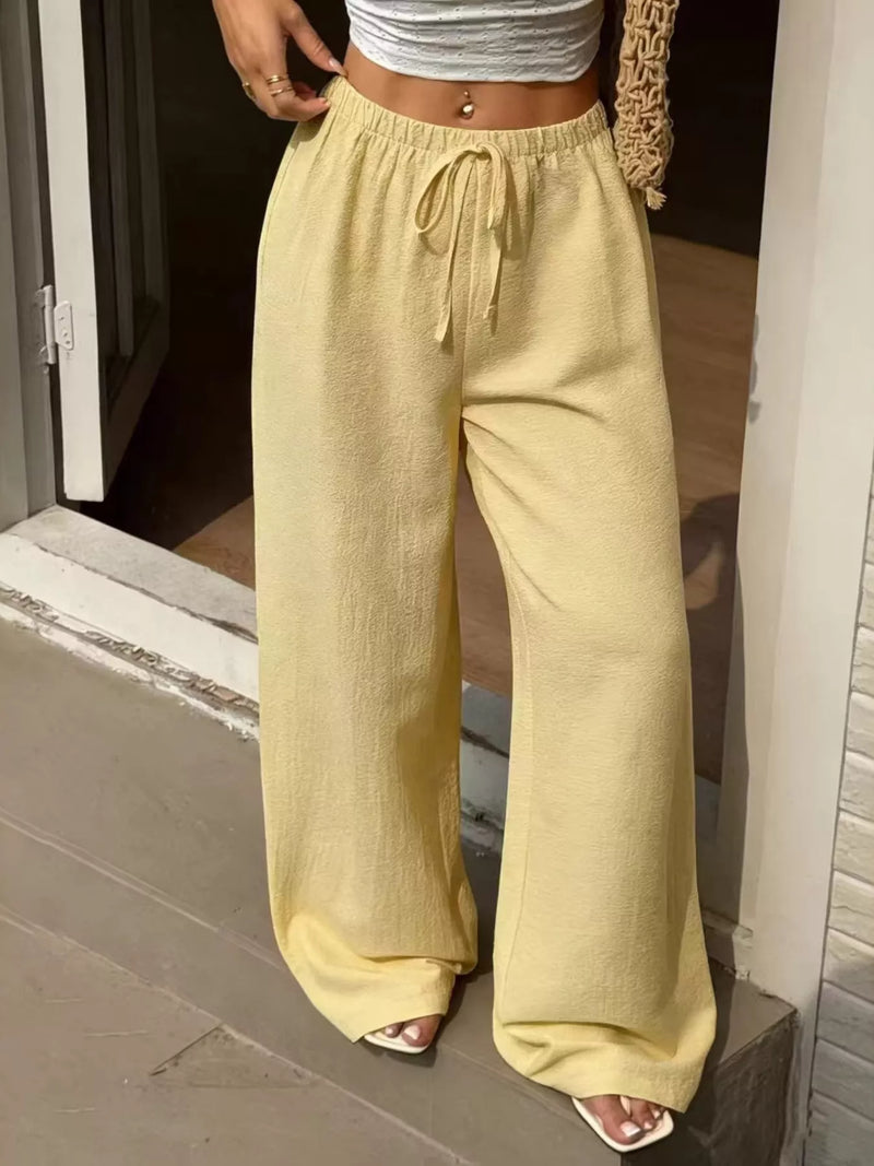 Person wearing light yellow wide-leg pants and a white top, standing indoors.