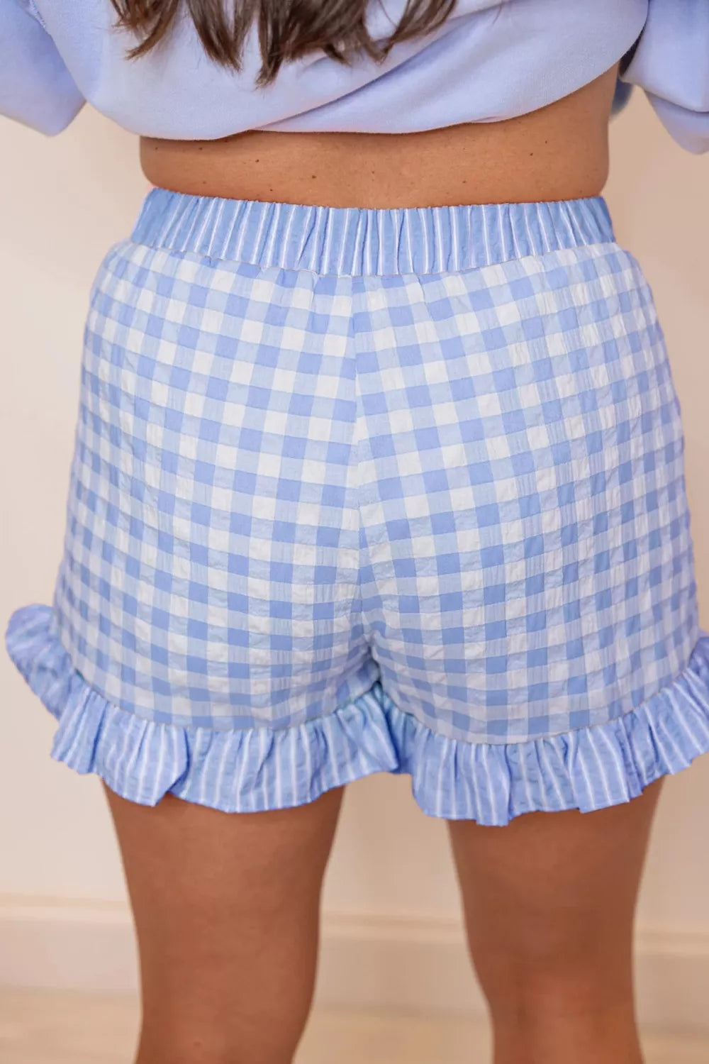 Blue and white checkered shorts with ruffle details on a neutral background