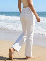 Person wearing white pants walking on a beach with ocean waves in the background