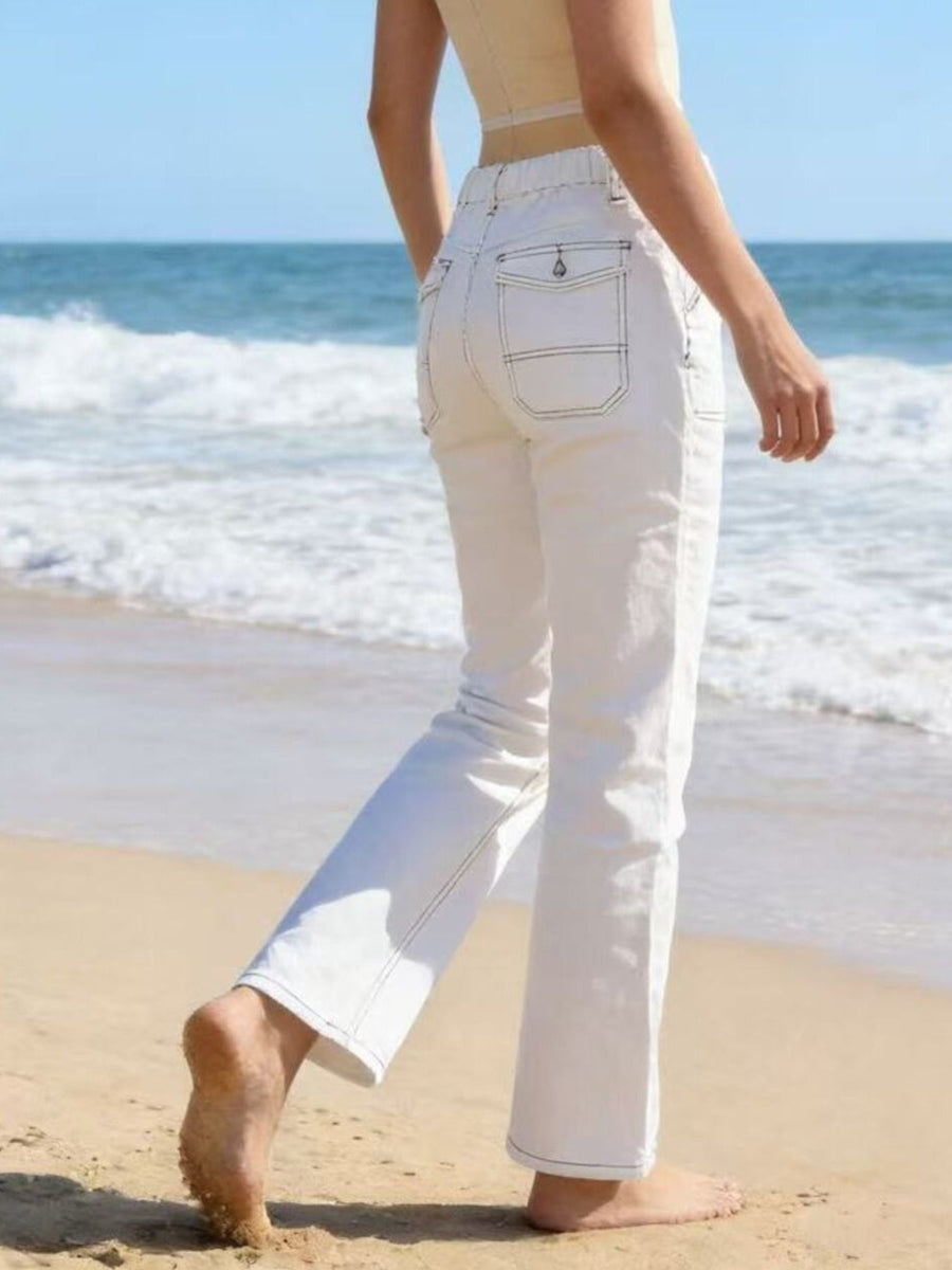 Person wearing white pants walking on a beach with ocean waves in the background