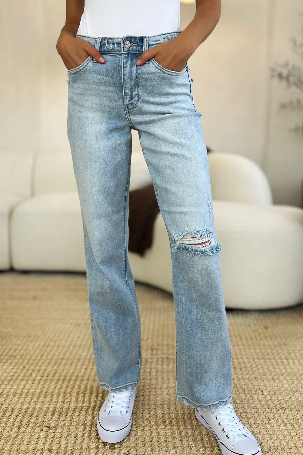 Person wearing light blue jeans with a slight distressed look, standing on a carpeted floor.