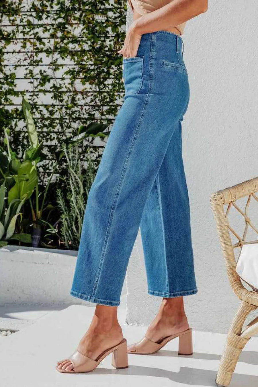 Person wearing blue jeans standing outdoors with plants and a chair in the background