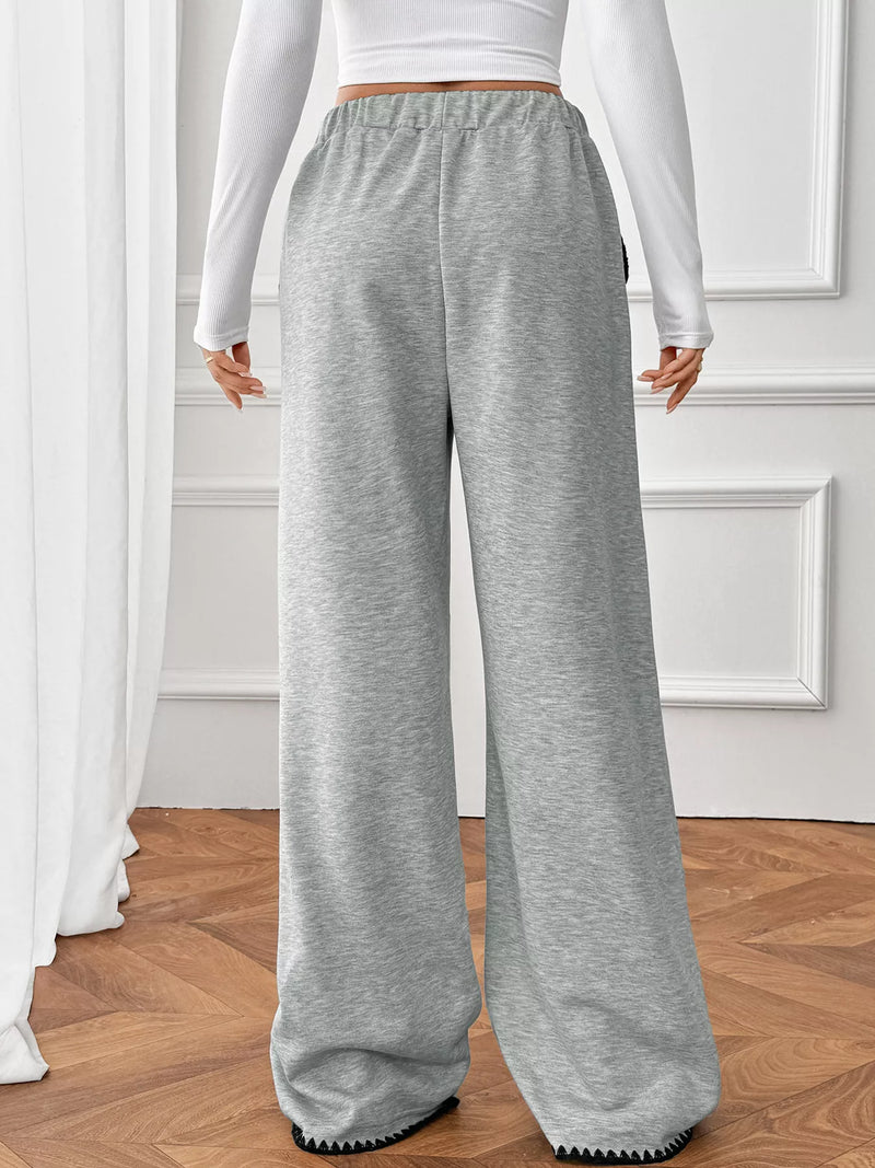 Person wearing gray sweatpants and a white long-sleeve top in a room with wooden flooring and white walls.