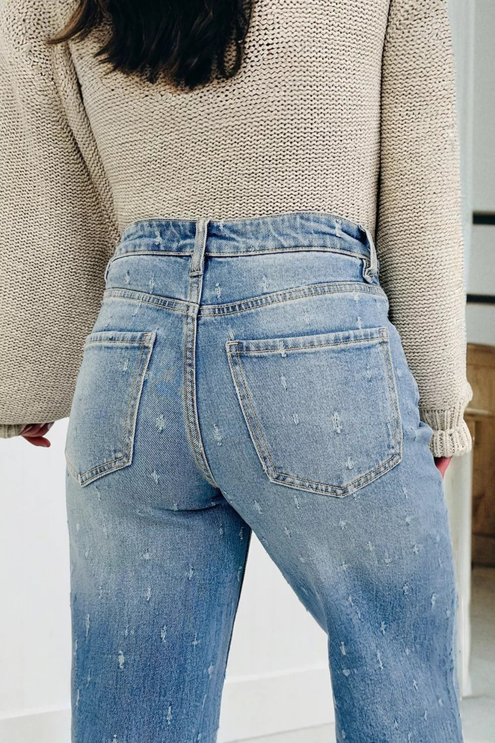 Person wearing light blue jeans and a beige sweater in an indoor setting