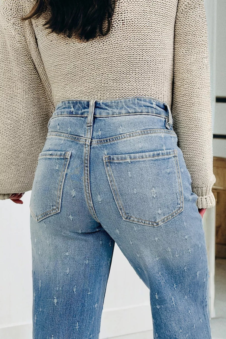 Person wearing light blue jeans and a beige sweater in an indoor setting