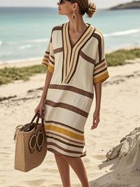 Woman in a striped beach cover-up with a straw bag on a sandy beach.