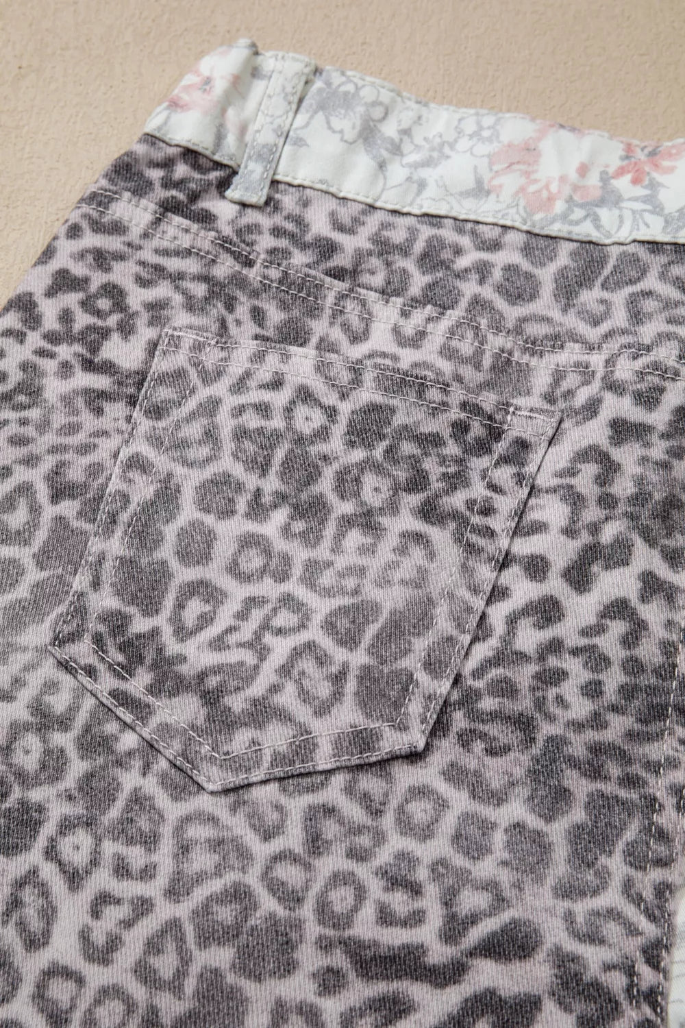 Leopard print denim shorts with floral lining on a beige background