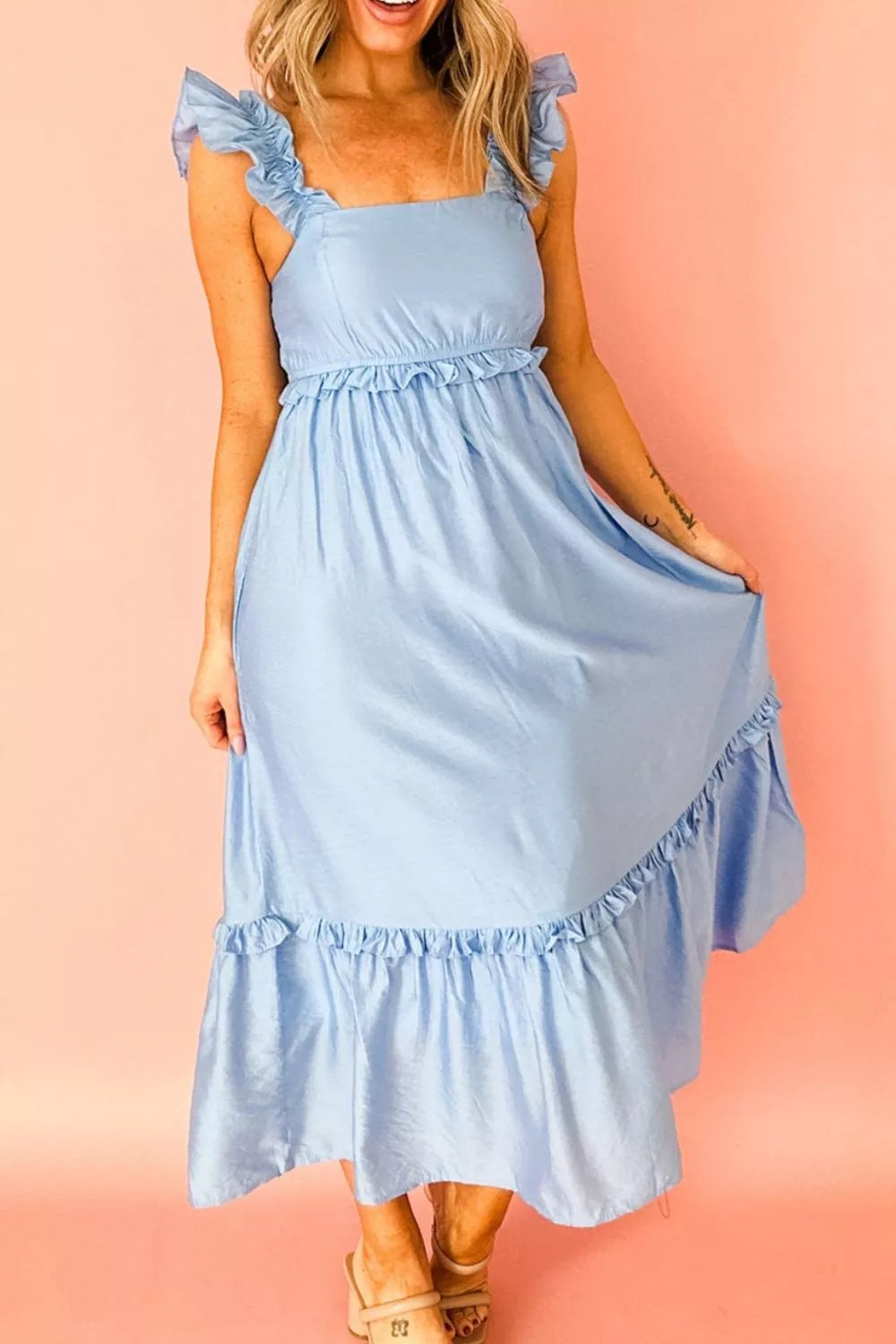 Woman wearing a light blue dress with ruffled straps and hem on a pink background