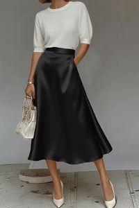 Person wearing a white top and black satin skirt with a gray background
