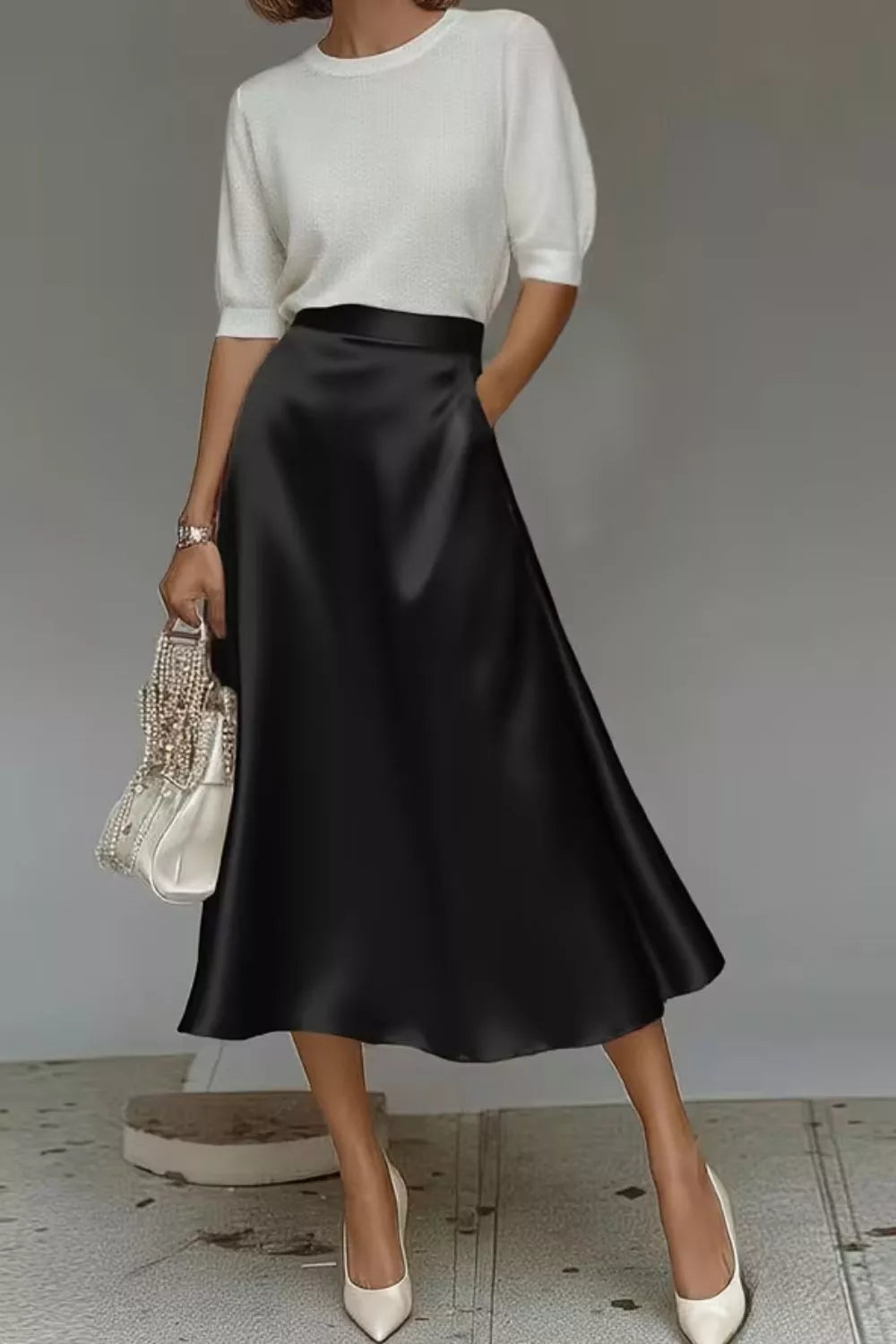 Person wearing a white top and black satin skirt with a gray background