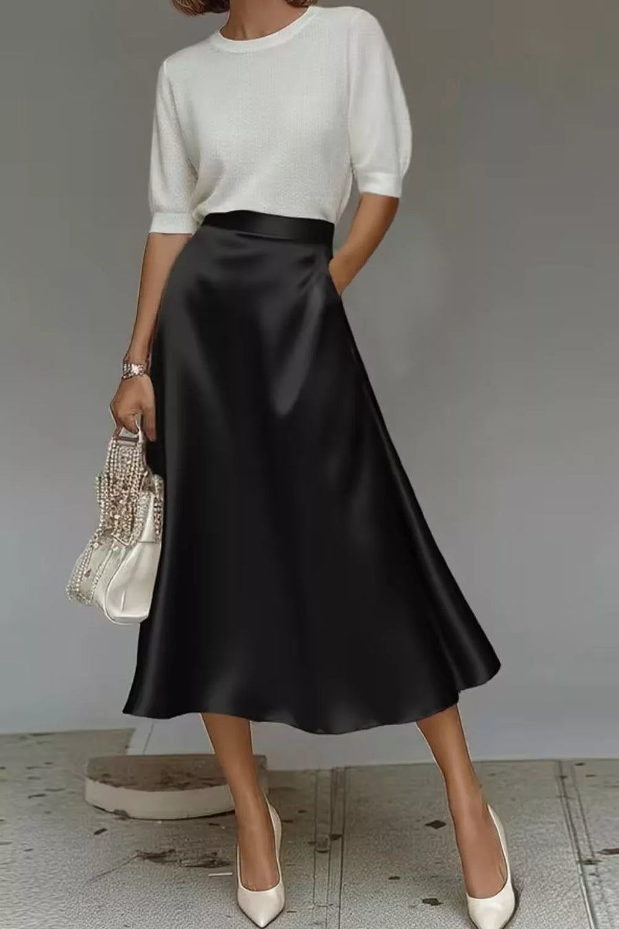 Person wearing a white top and black satin skirt with a gray background