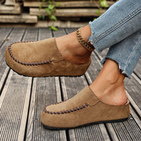 Brown suede loafers worn with light blue jeans on a wooden floor.