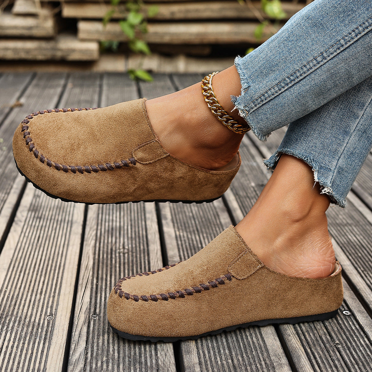 Brown suede loafers worn with light blue jeans on a wooden floor.