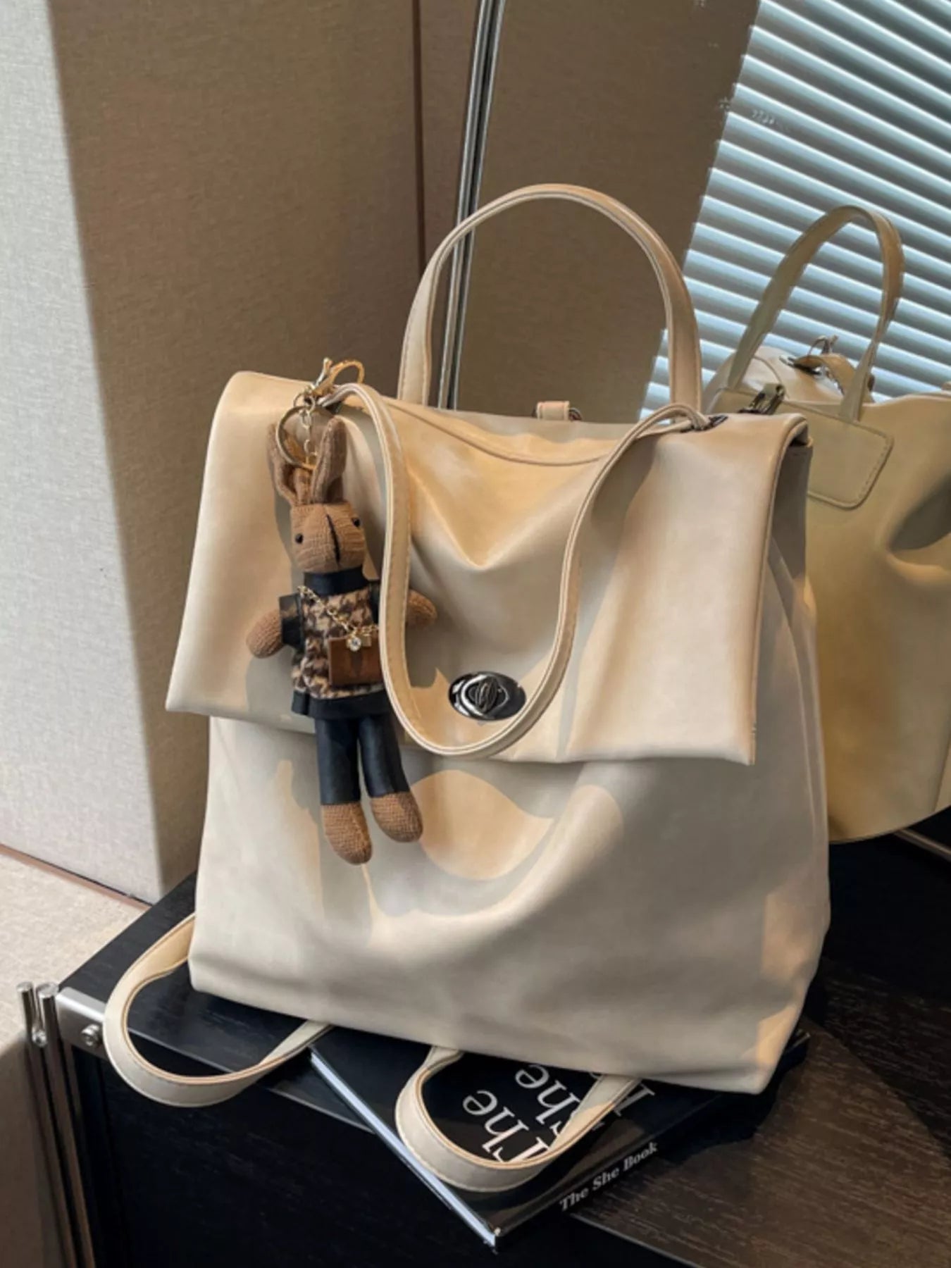 Beige handbag with a teddy bear keychain on a surface