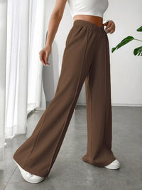 Person wearing brown wide-leg pants and white top in a minimalistic room.