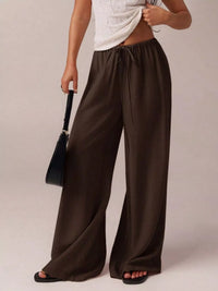Person wearing brown wide-leg pants holding a black handbag on a plain background