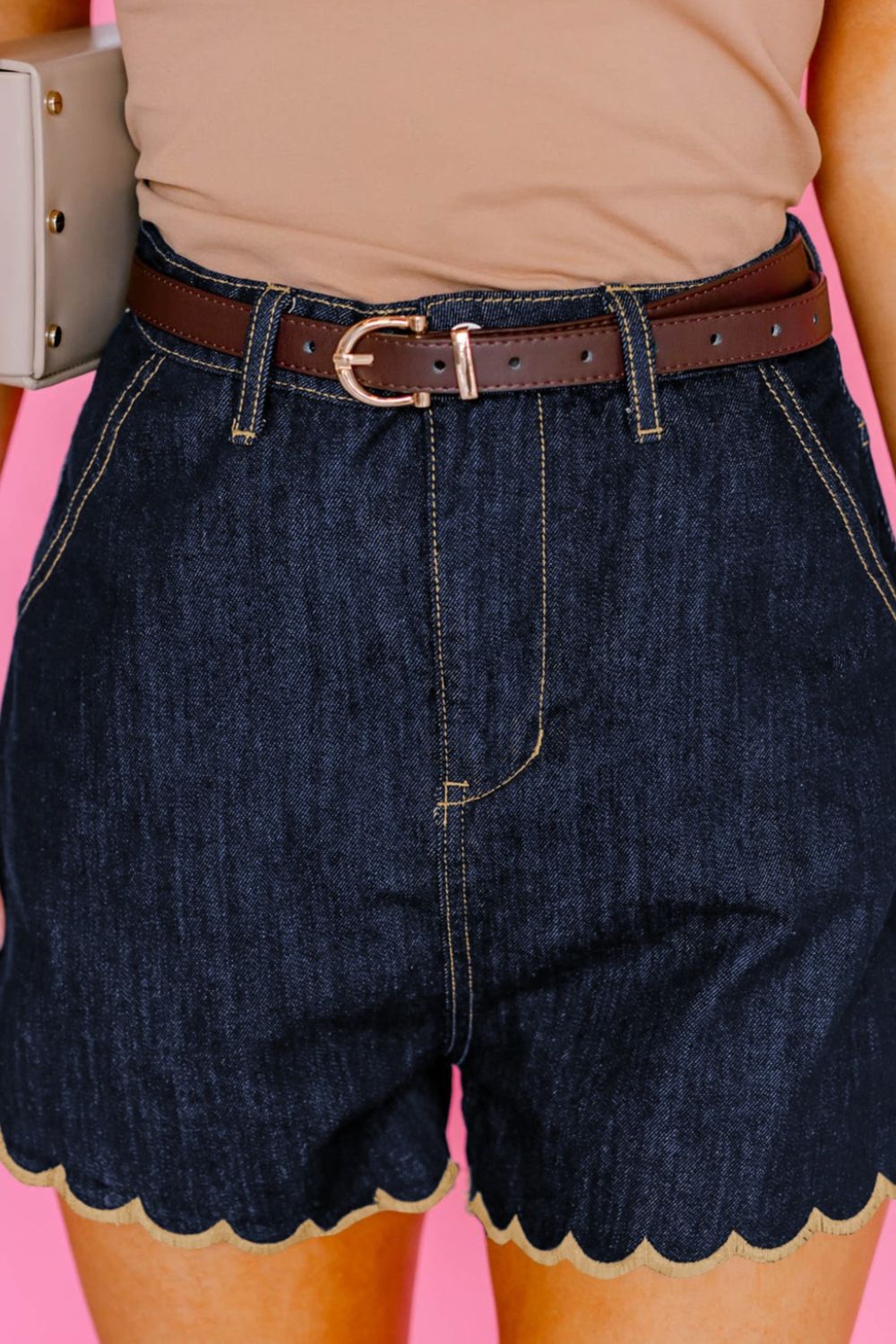 Person wearing dark blue denim shorts with scalloped hem on a pink background