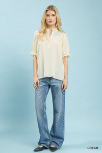 Woman wearing a cream blouse and blue jeans against a light blue background