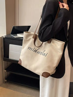 Person holding a beige tote bag with 'miduolai' branding in an indoor setting.