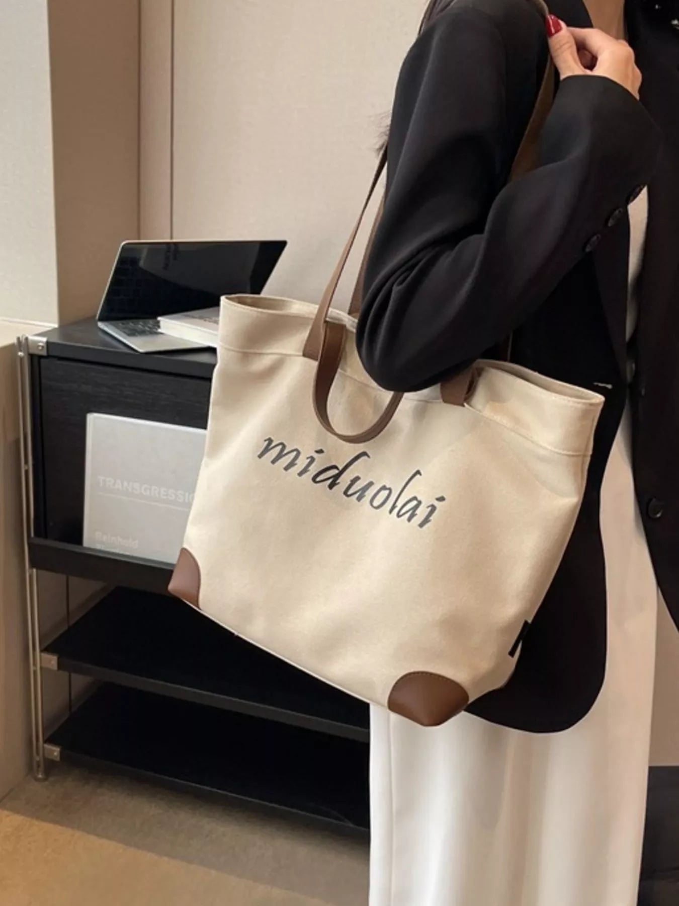 Person holding a beige tote bag with 'miduolai' branding in an indoor setting.