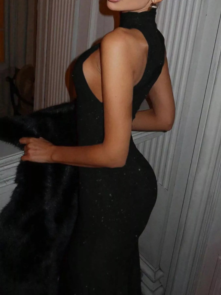 Person wearing a black dress with a high neckline and open back, standing against a neutral background.