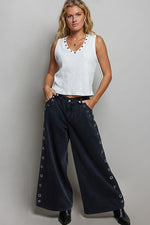 Woman wearing a white sleeveless top and black pants with decorative elements on a gray background