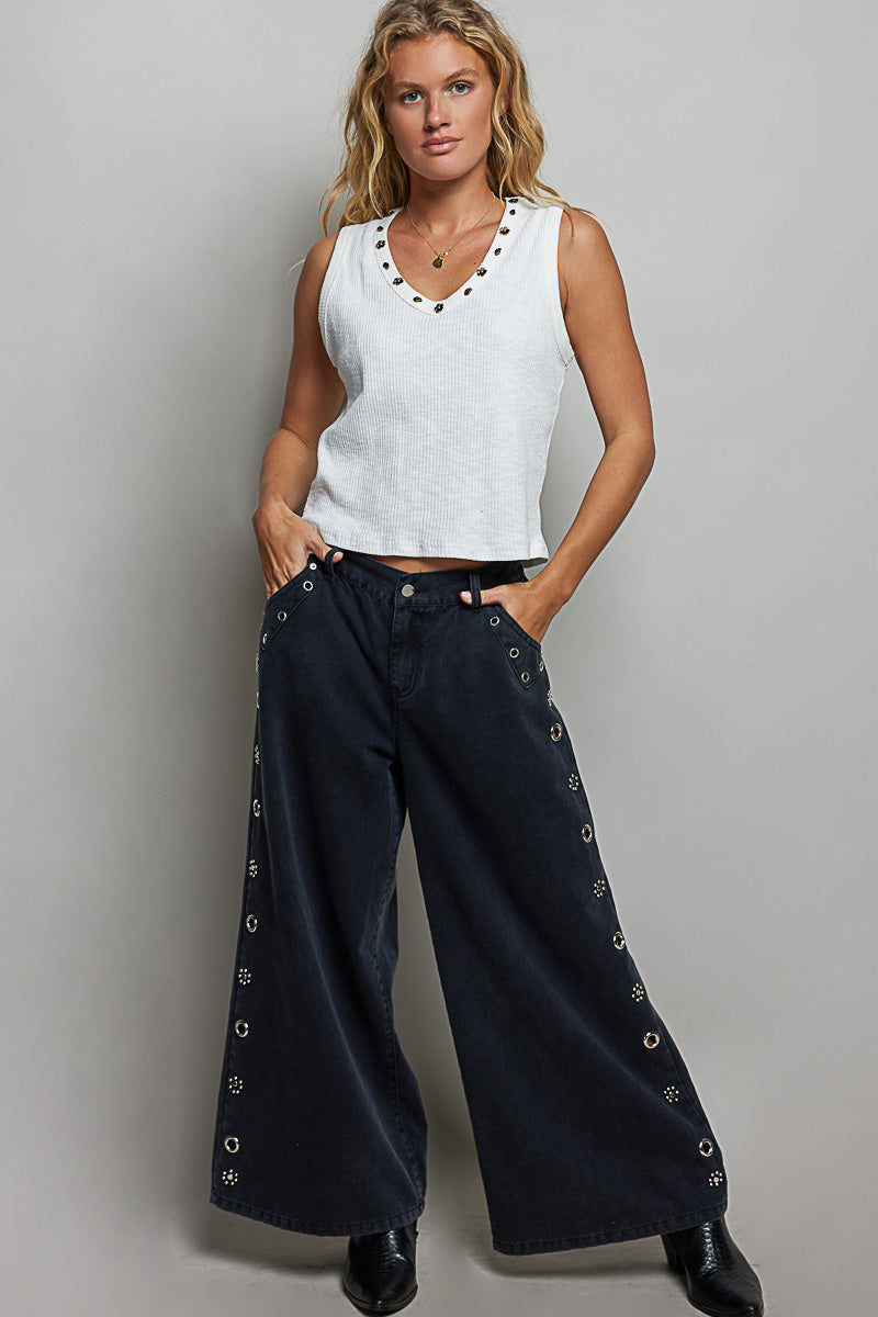 Woman wearing a white sleeveless top and black pants with decorative elements on a gray background
