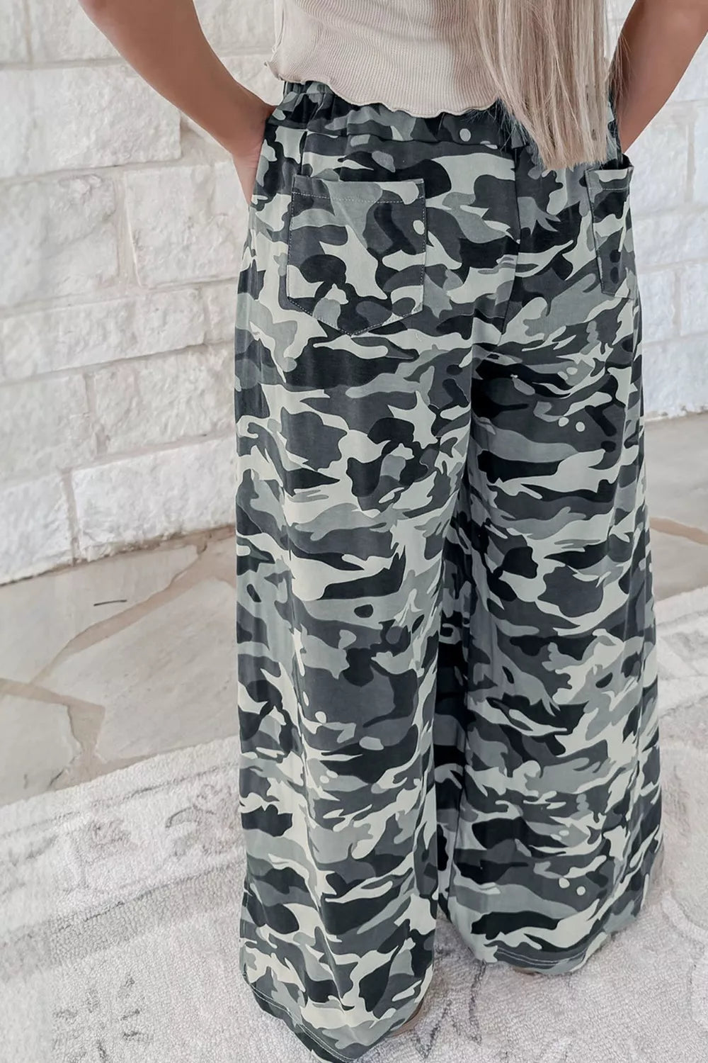 Camouflage pants worn by a person against a light stone wall.