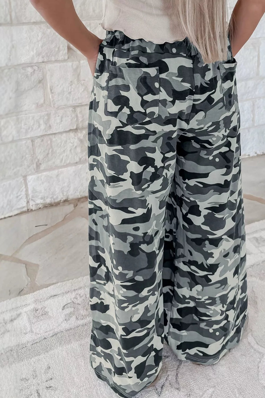 Camouflage pants worn by a person against a light stone wall.