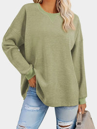 Person wearing a green sweater and ripped jeans on a white background