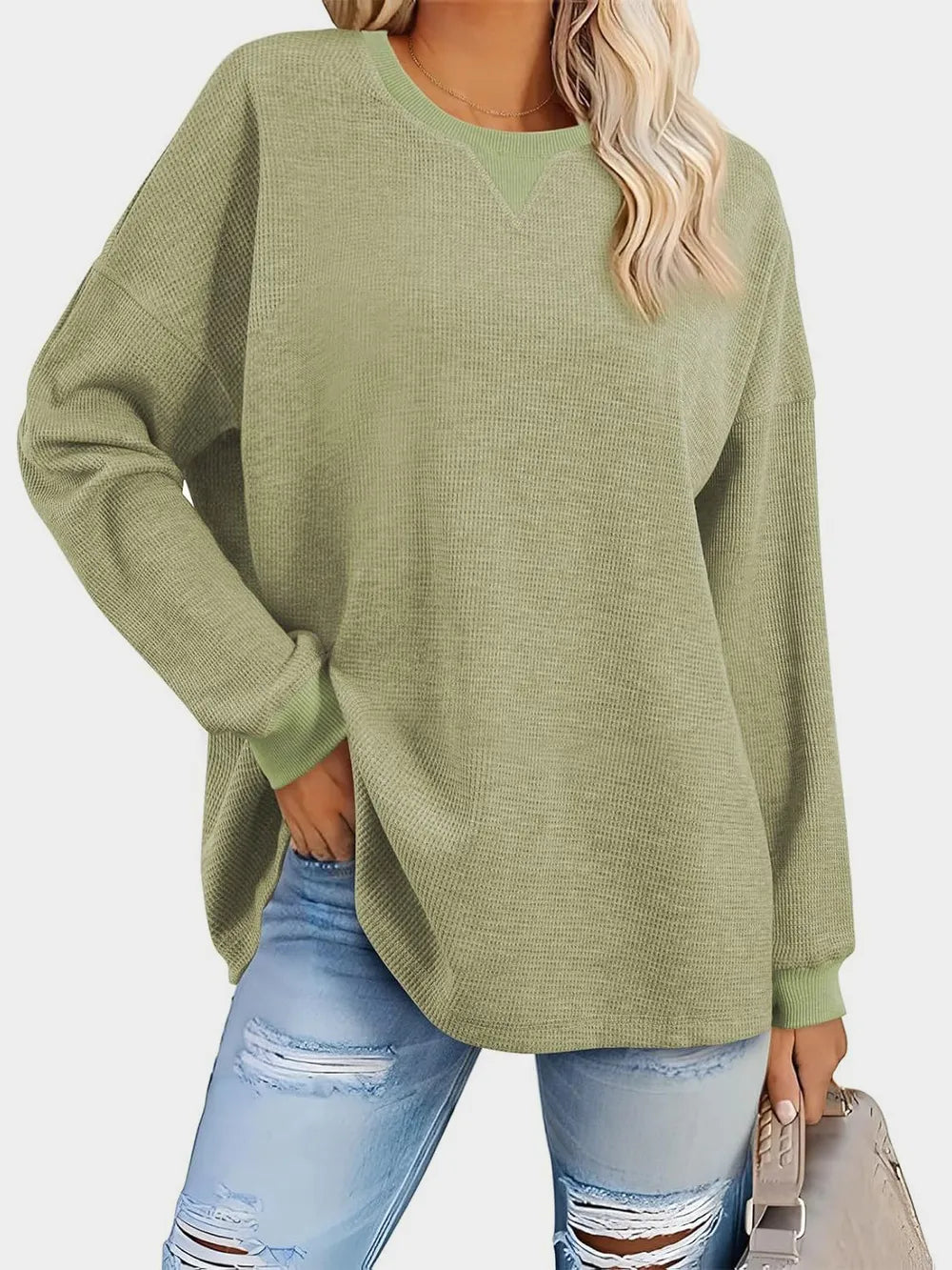 Person wearing a green sweater and ripped jeans on a white background