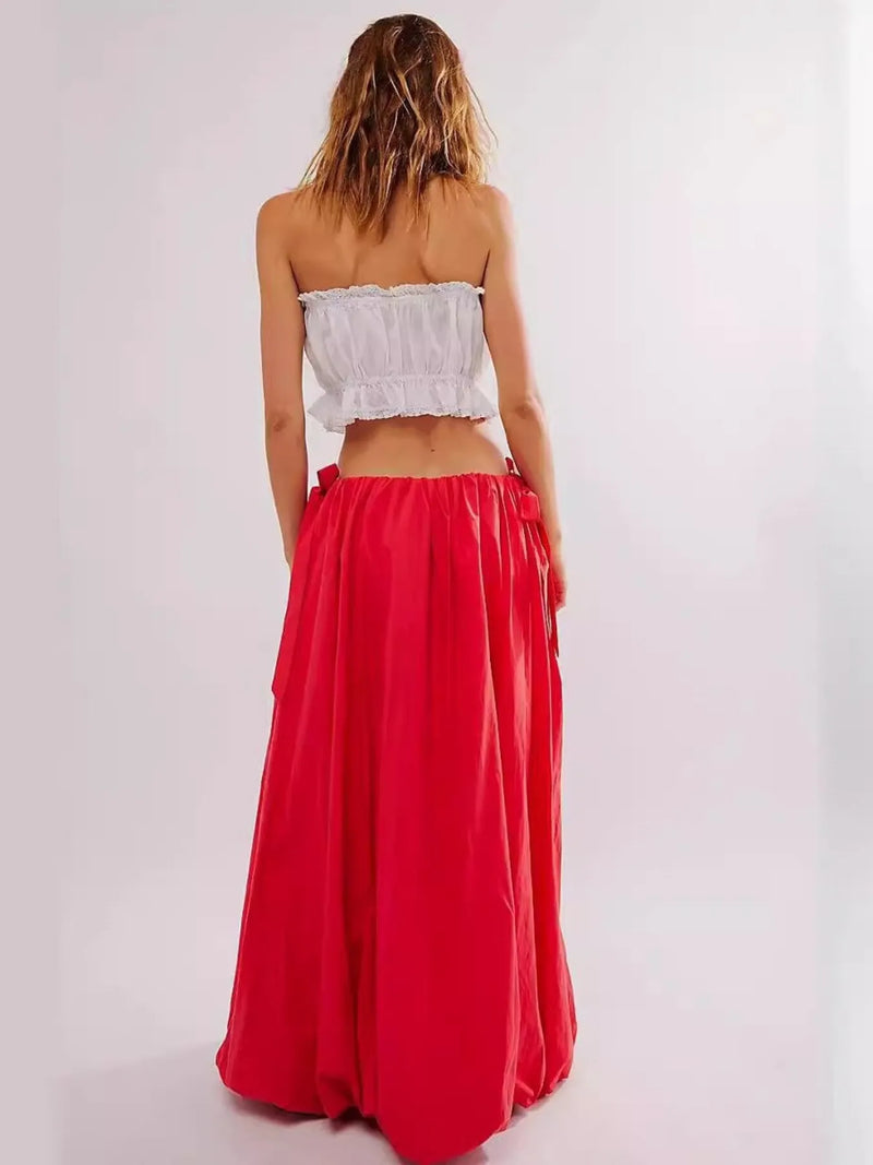 Person wearing a white strapless top and red skirt on a plain background