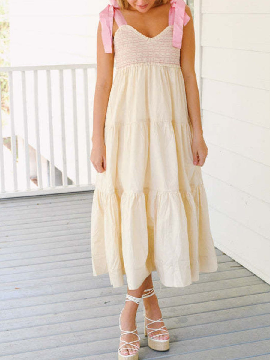 Woman wearing a cream dress with pink ribbons on a wooden deck